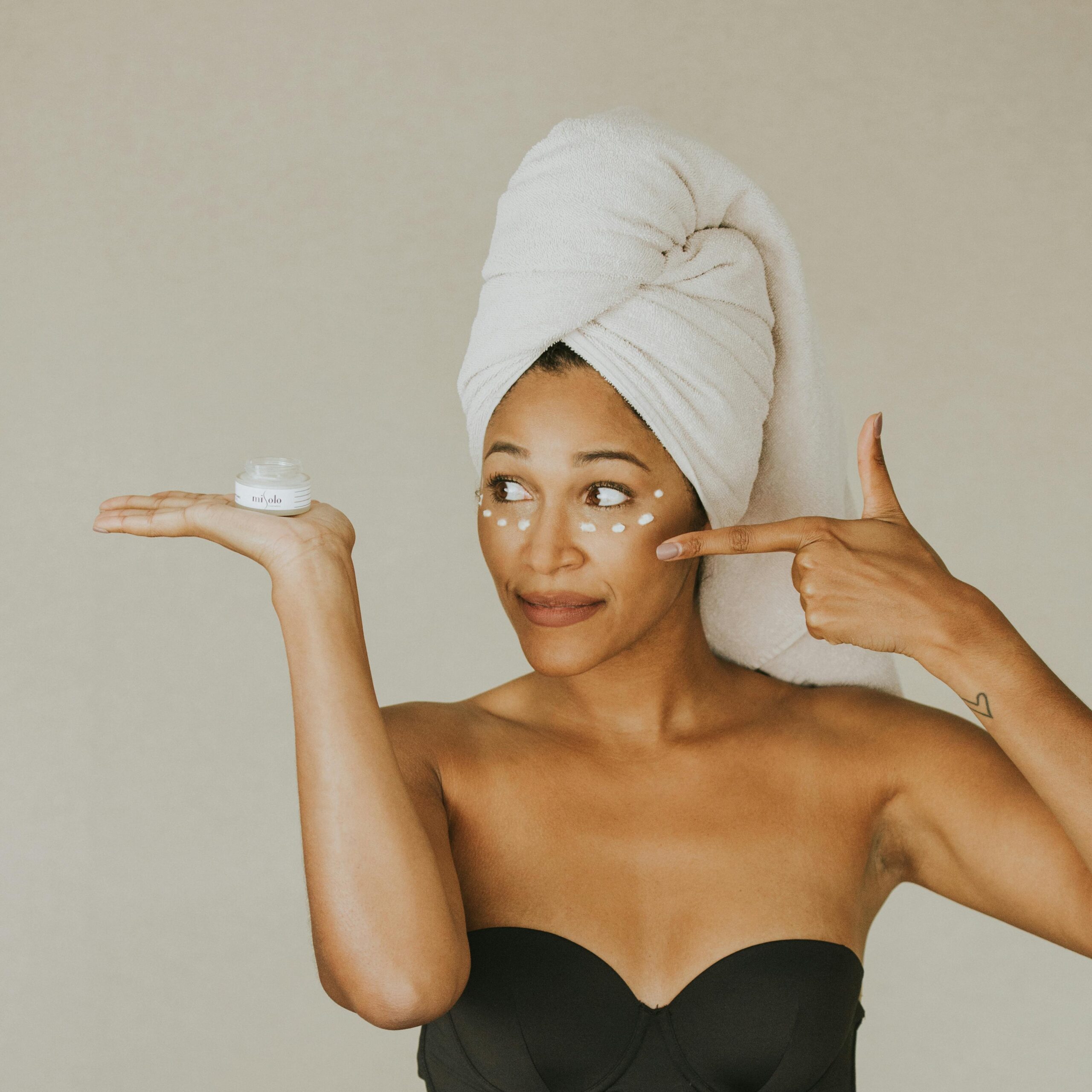 Woman in towel wrap applying face cream, highlighting skincare routine.