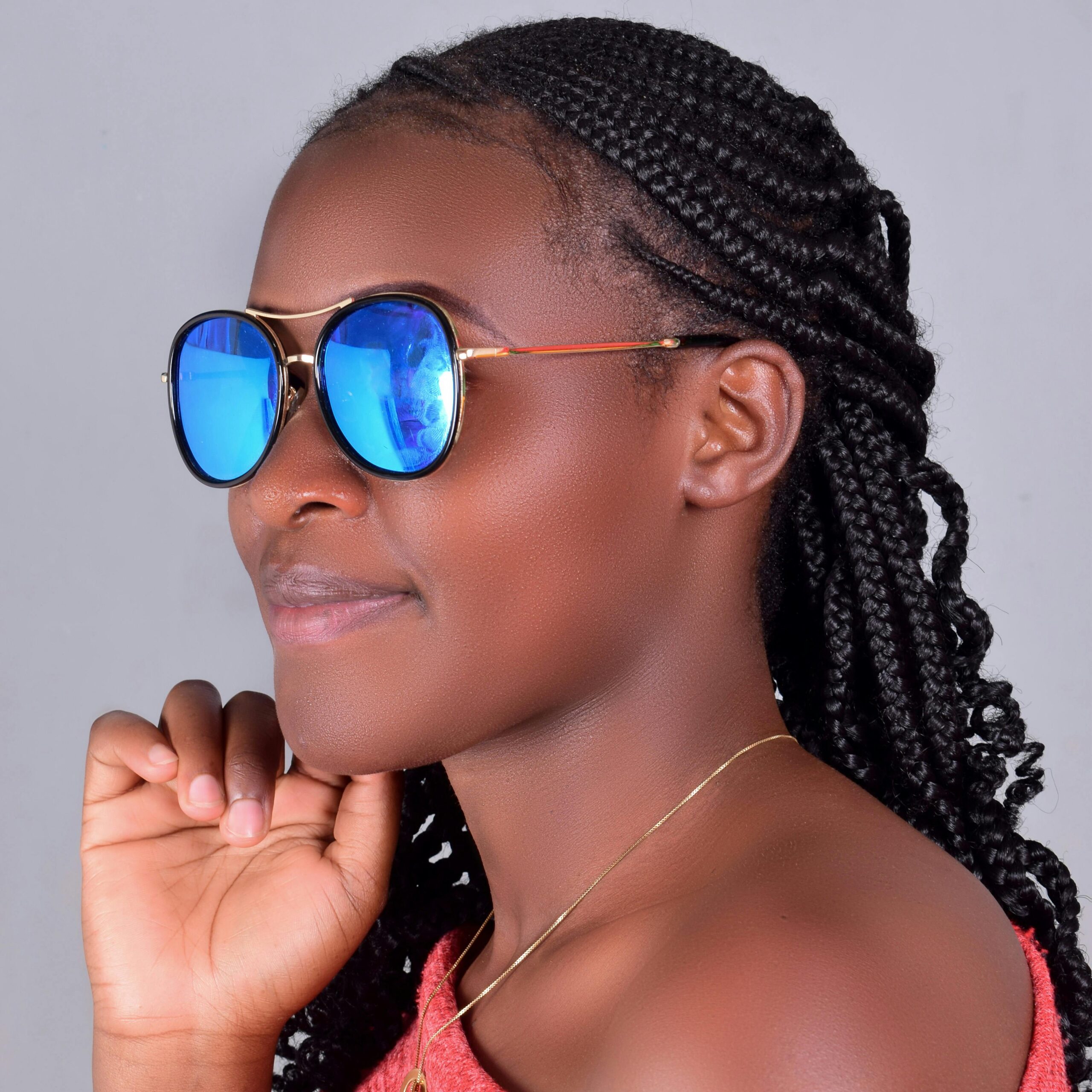 Portrait of a stylish woman with braided hair and reflective sunglasses against a neutral background.
