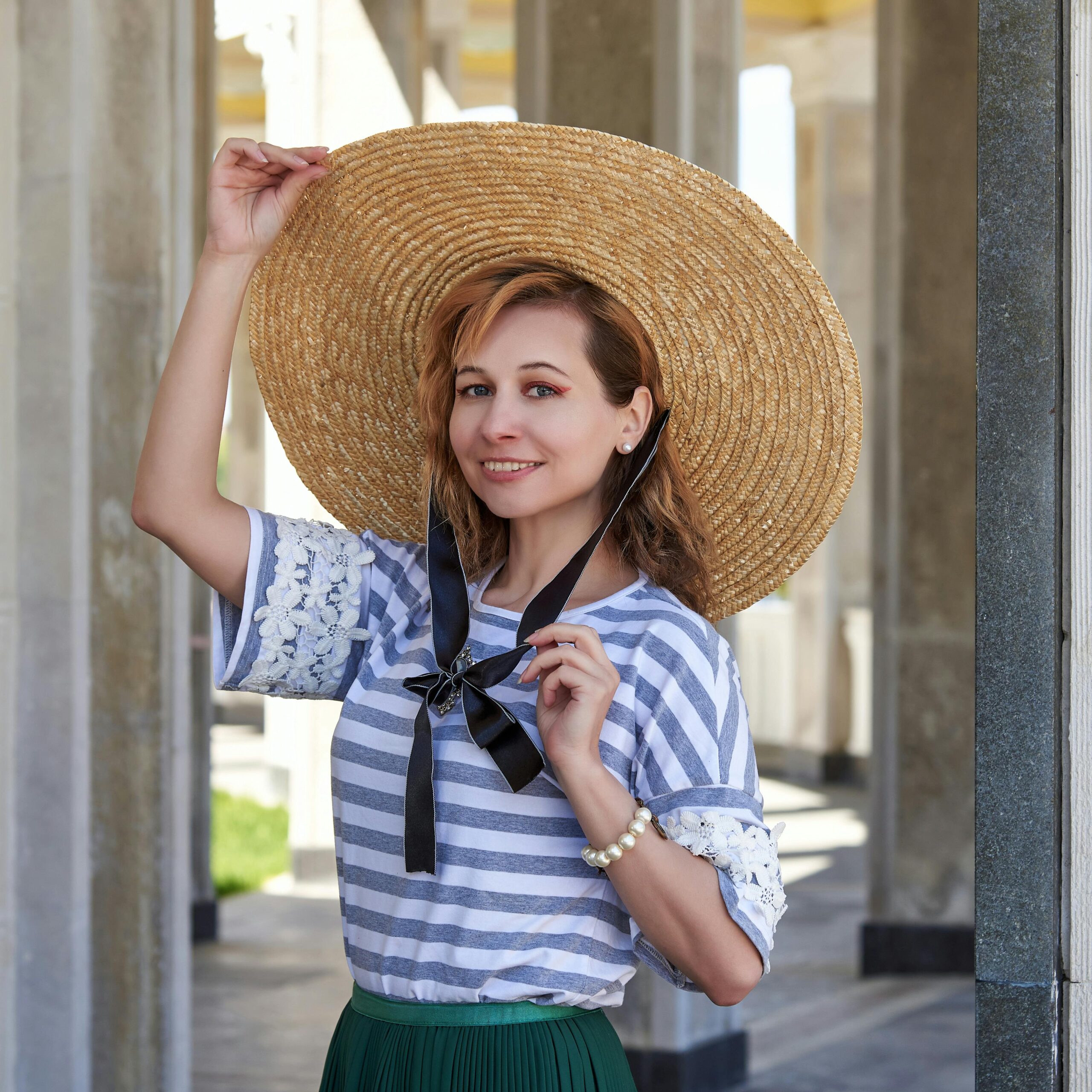 Smiling woman outdoors in summer fashion wearing a striped shirt and straw hat.