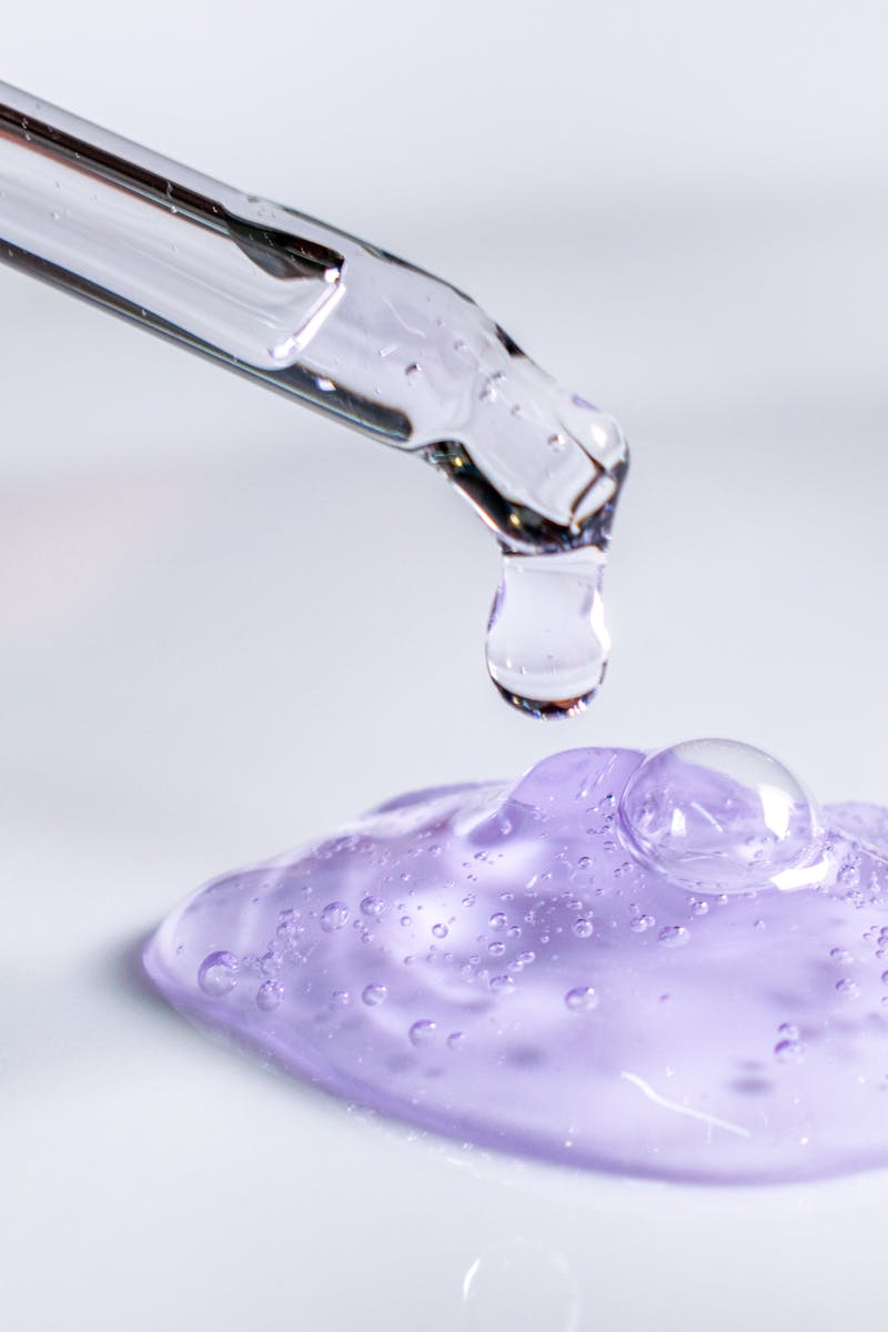 Pipette releasing drop of purple gel, highlighting skincare and laboratory use.