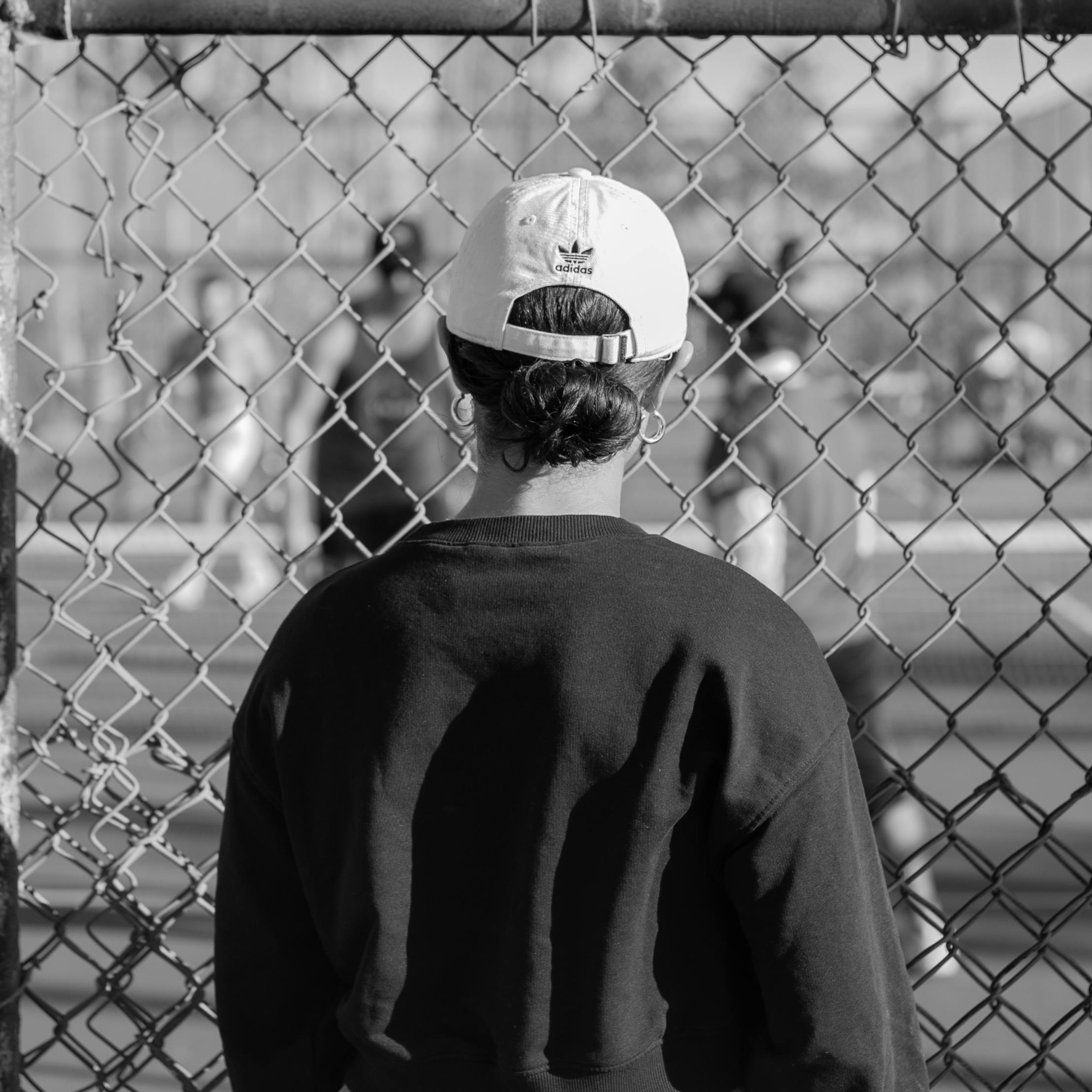 Monochrome shot of a person in a cap looking through a fence at Santa Monica.
