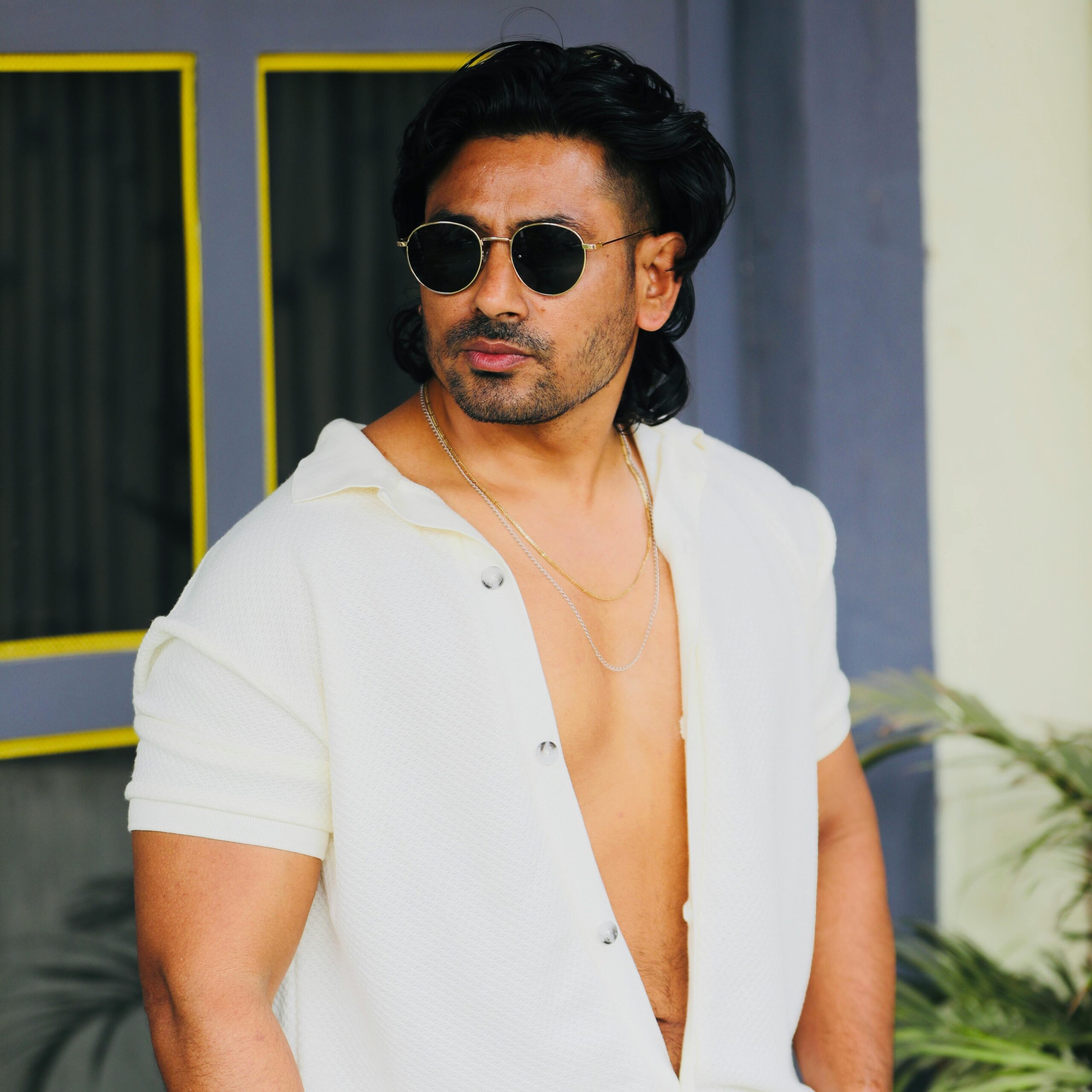 Confident man dressed in a stylish summer outfit, wearing sunglasses in a casual pose.