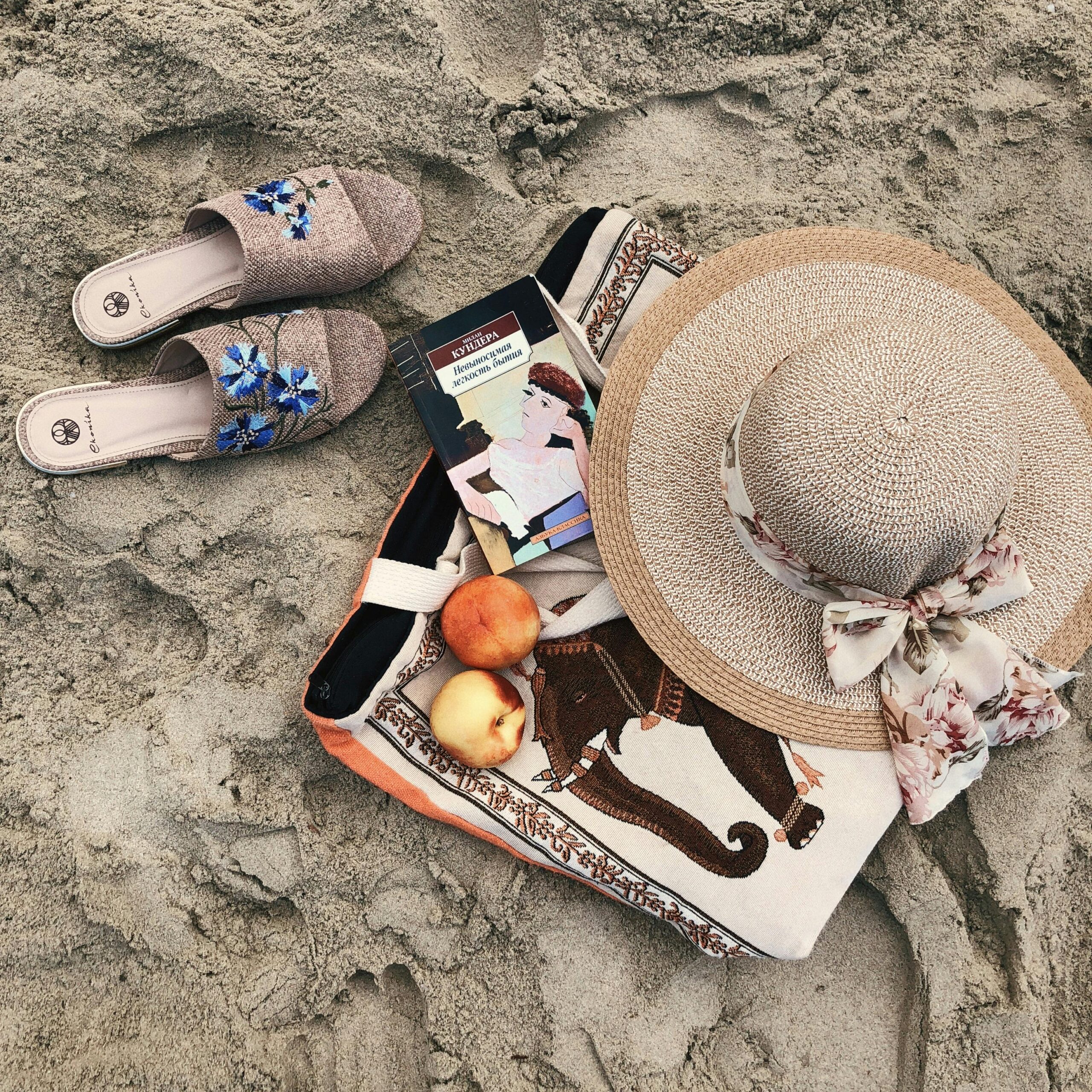 Flat lay of beach essentials with hat and slippers on sand. Perfect summer vibe.