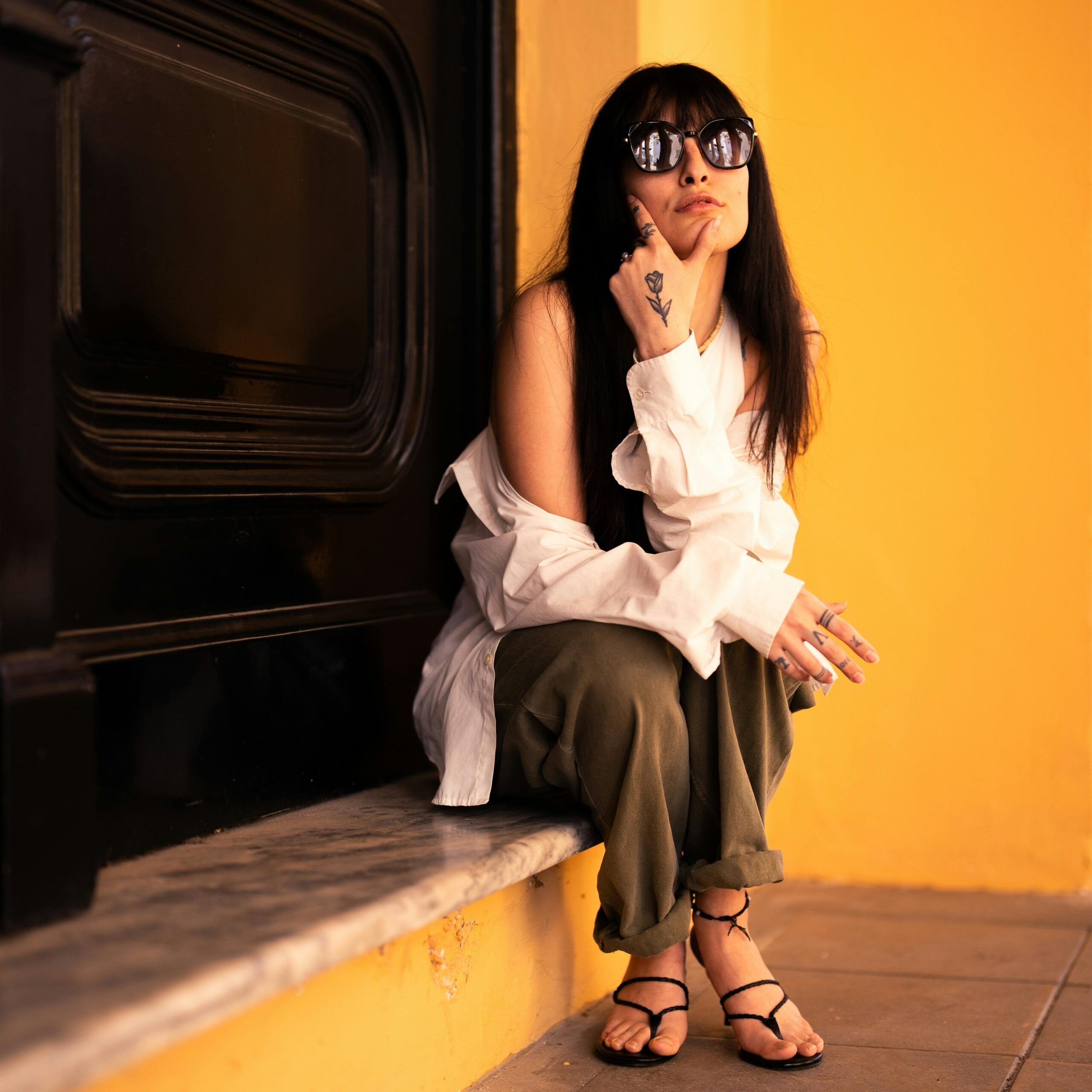 Fashionable woman in casual attire and sunglasses sitting on a marble ledge.