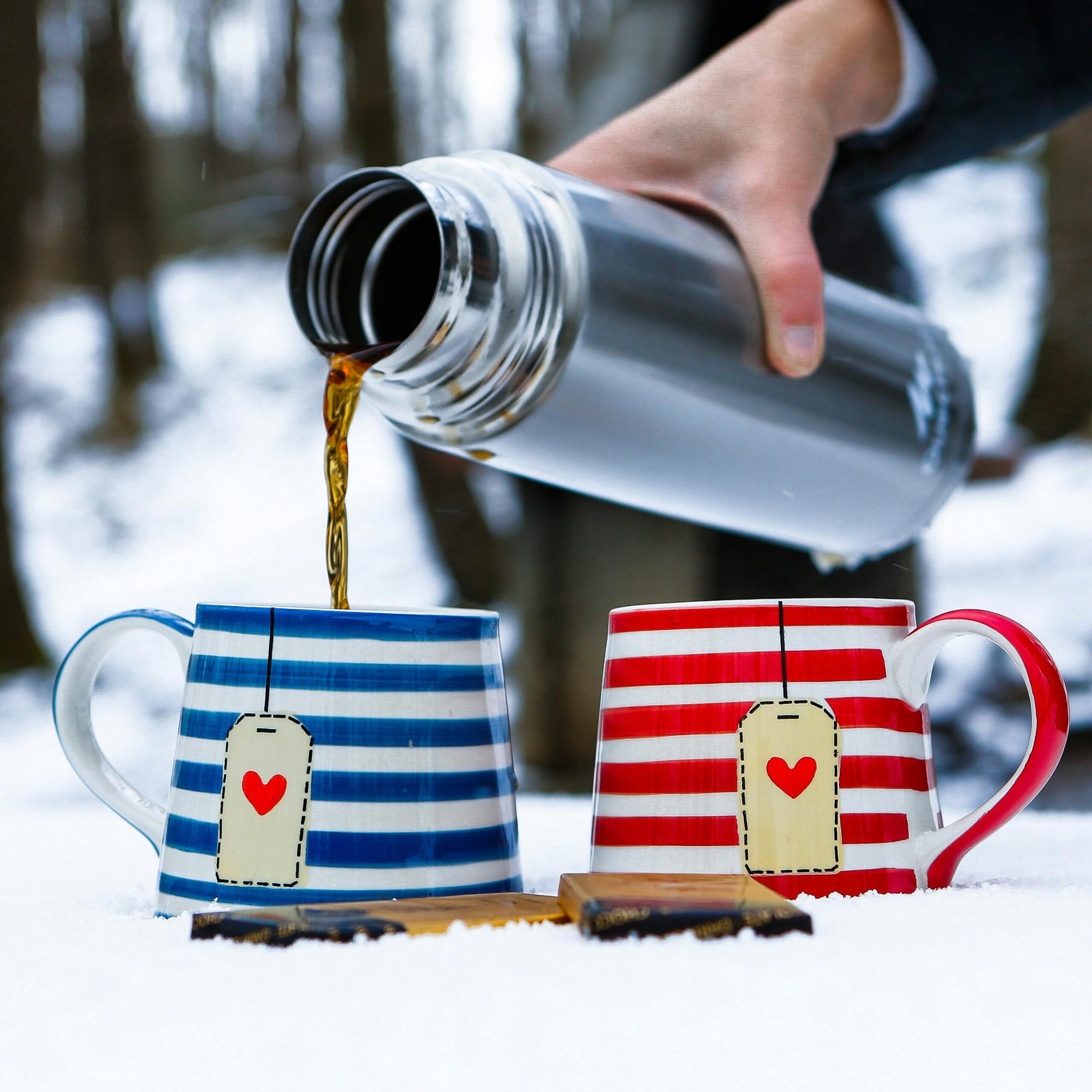 A warm drink poured from a thermos into striped mugs on snow, İstanbul winter scene.