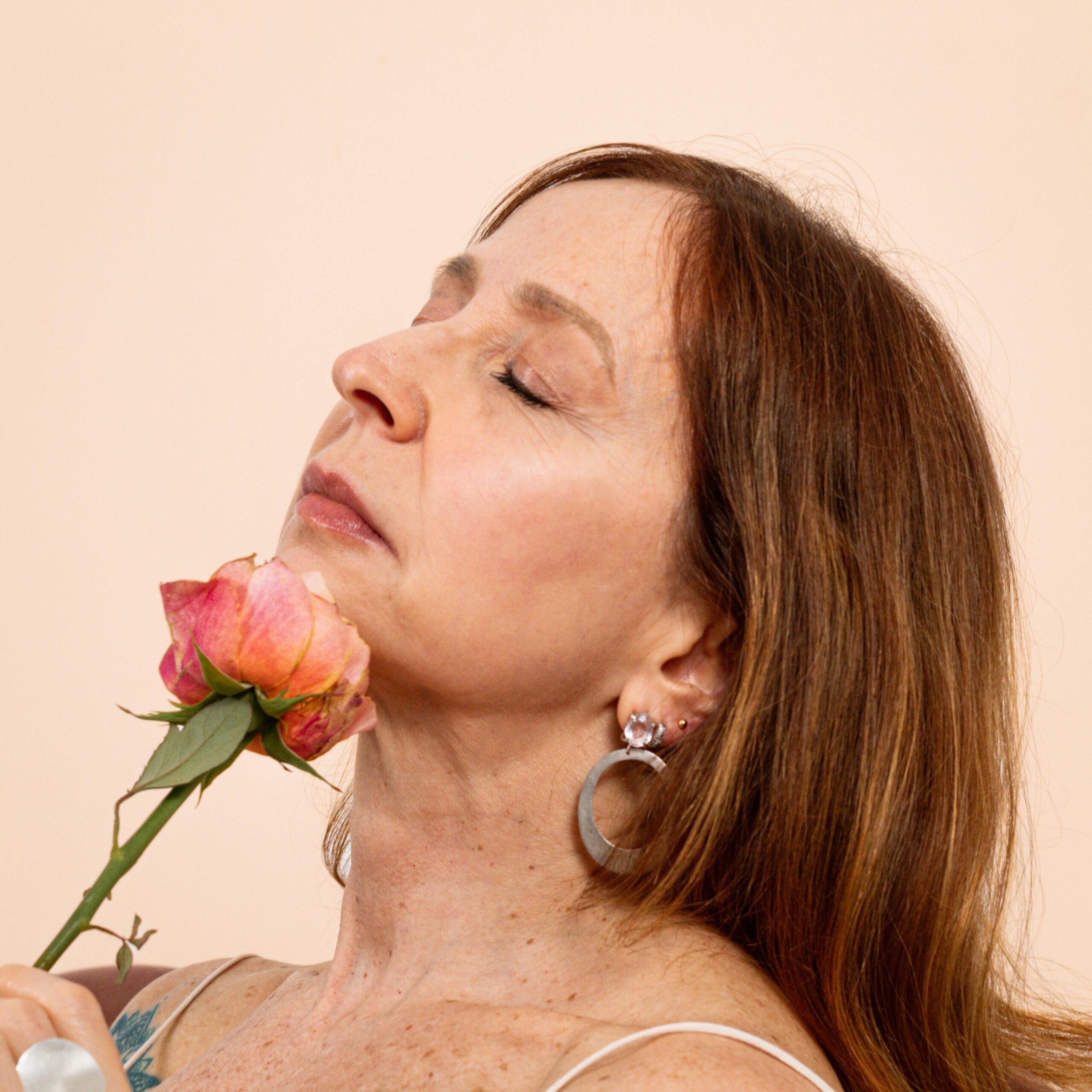 Close-up portrait of an adult woman gently holding a pink rose, exuding elegance and serenity.