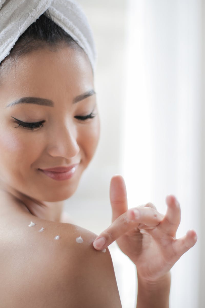 A young woman applying moisturizer indoors, enhancing skin care routine.