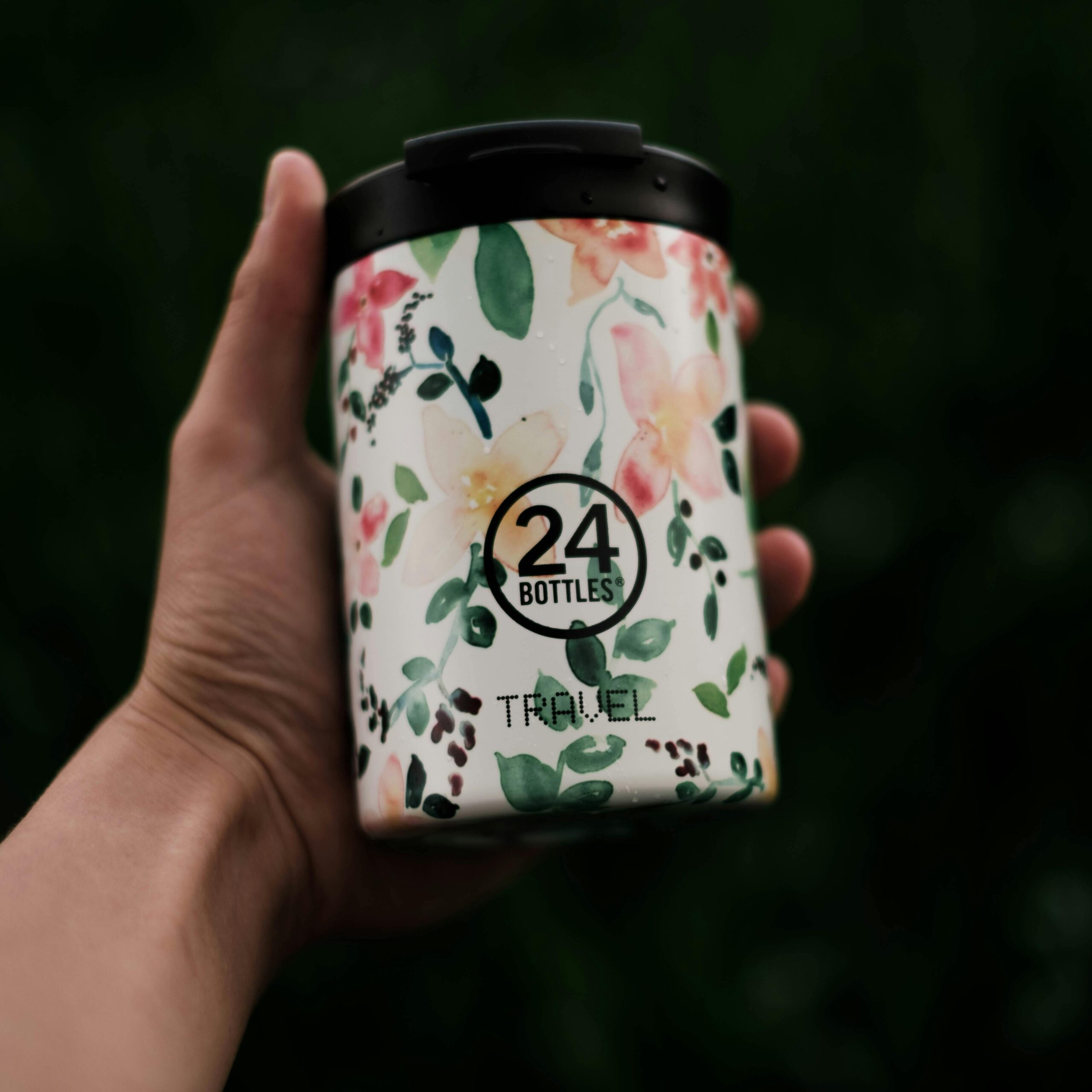 Crop anonymous person holding reusable ceramic bottle for water against blurred background of greenery