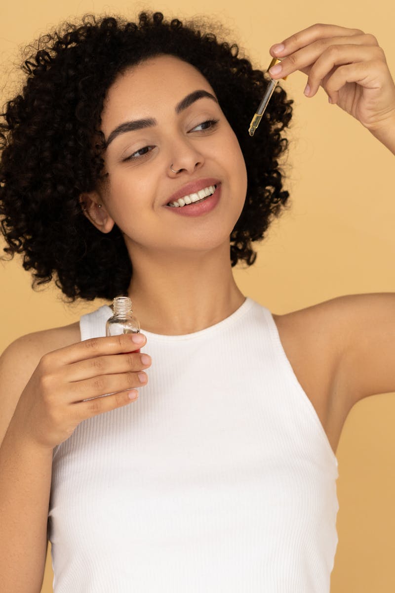 A smiling woman with curly hair applying essential oil for healthy skin care.