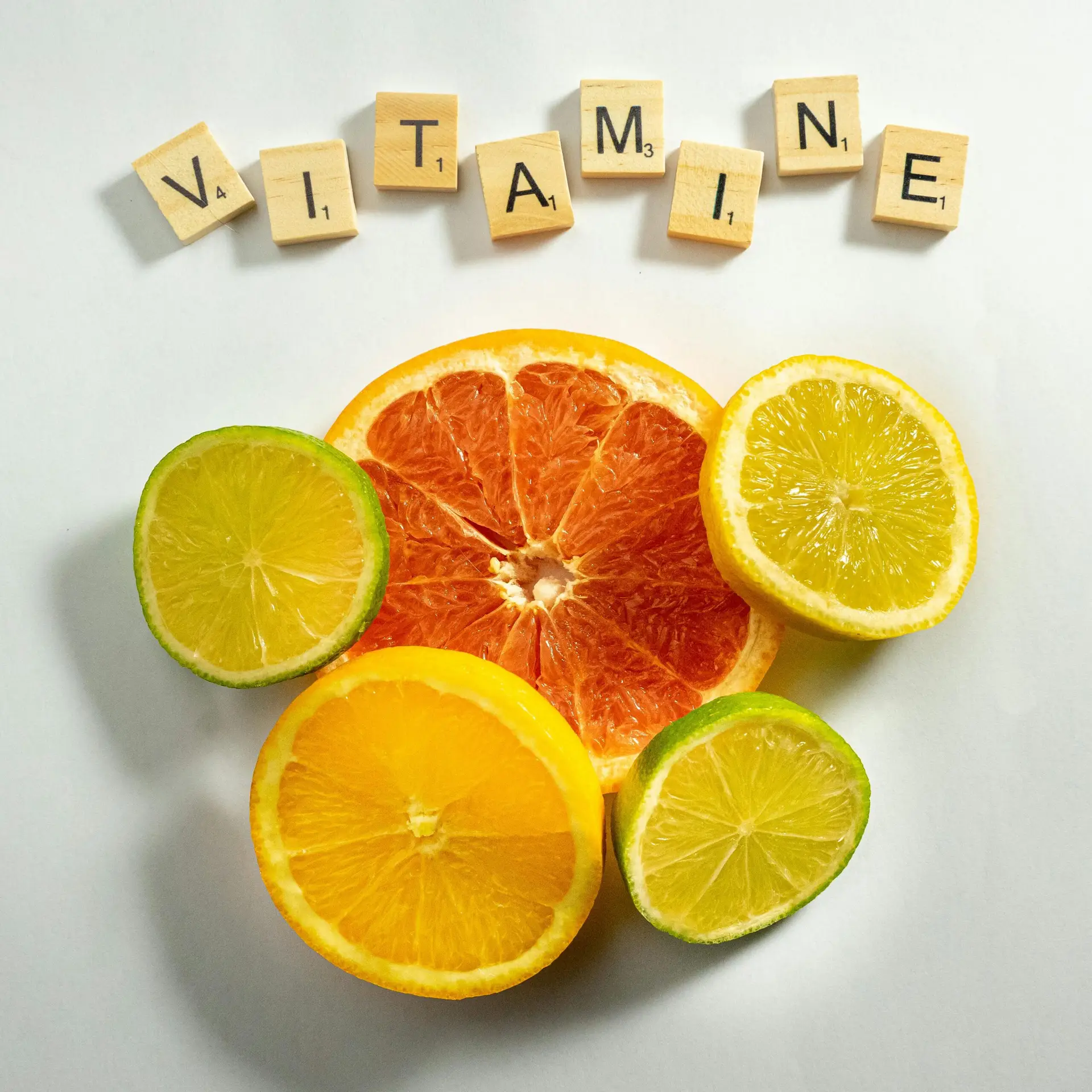 Vibrant citrus fruits arranged with scrabble tiles spelling 'VITAMIN E'. Bright and fresh composition.