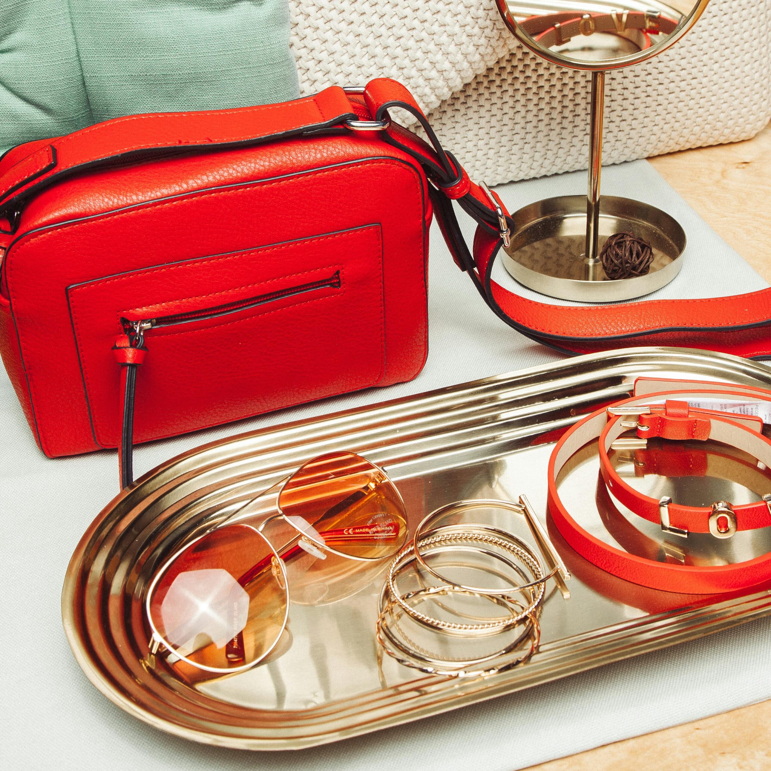 Stylish red handbag with matching accessories on a tray, perfect for a chic fashion statement.