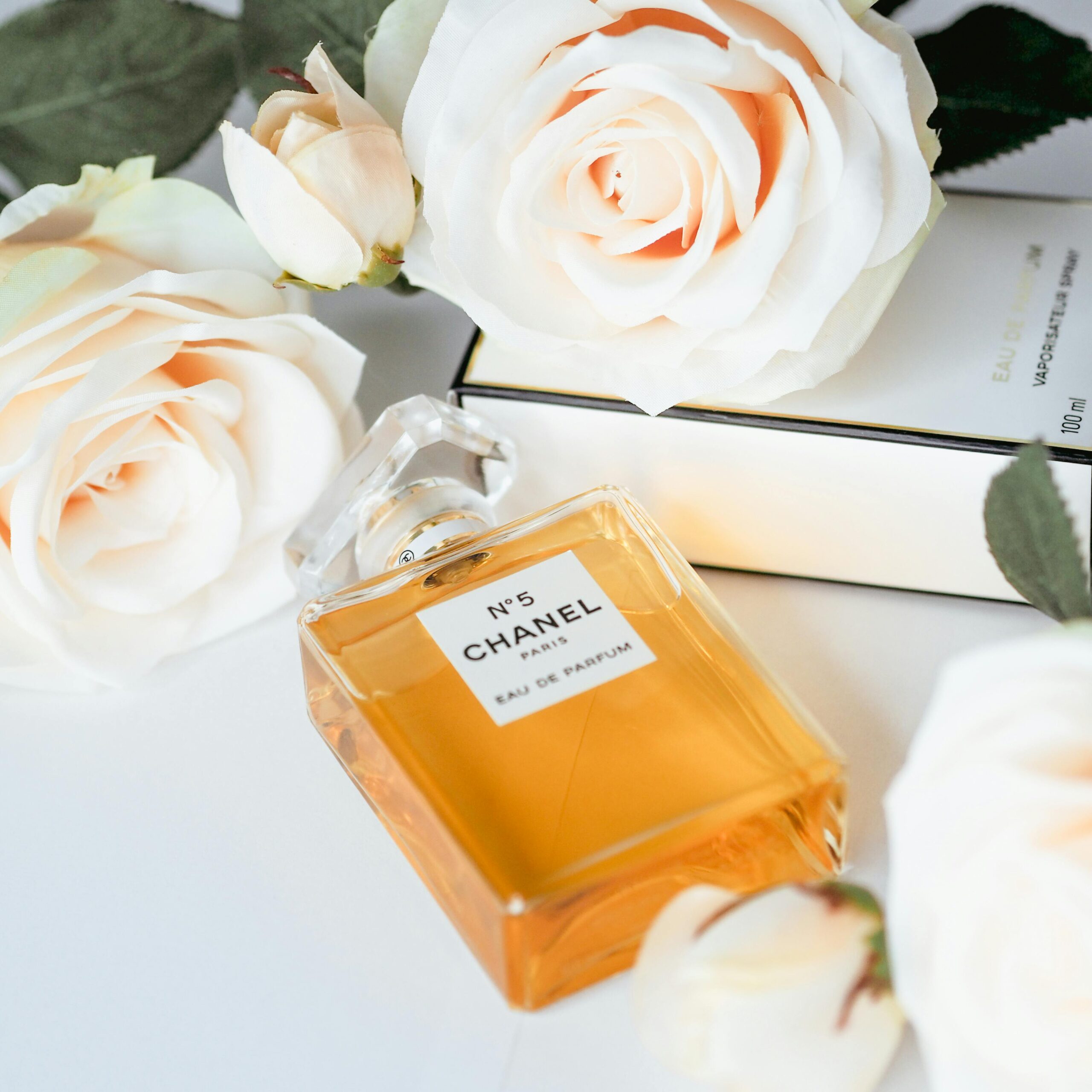 Chanel No 5 perfume bottle elegantly surrounded by white roses, symbolizing luxury.