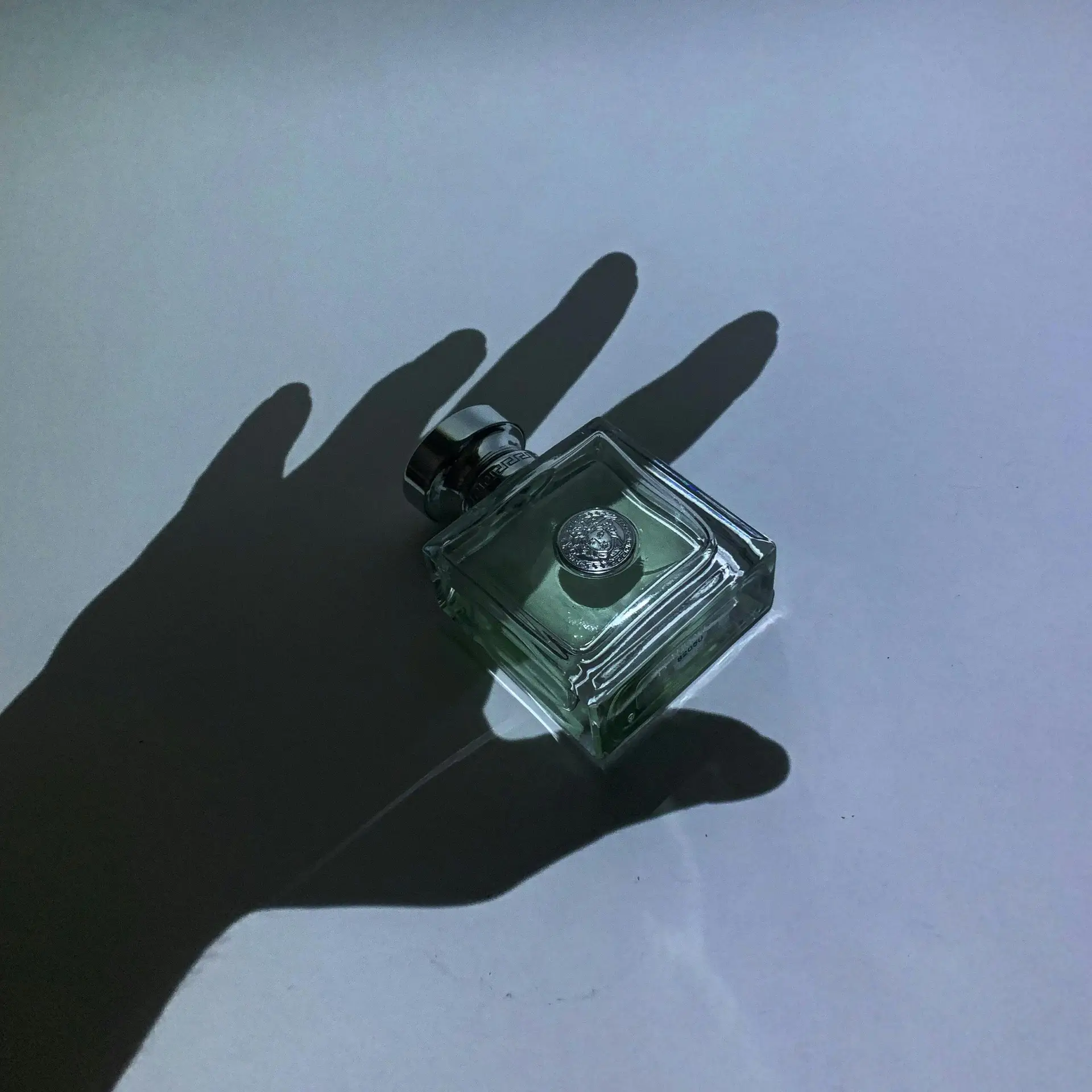 Elegant composition featuring a perfume bottle with dramatic hand shadows, creating a mysterious and artistic effect.
