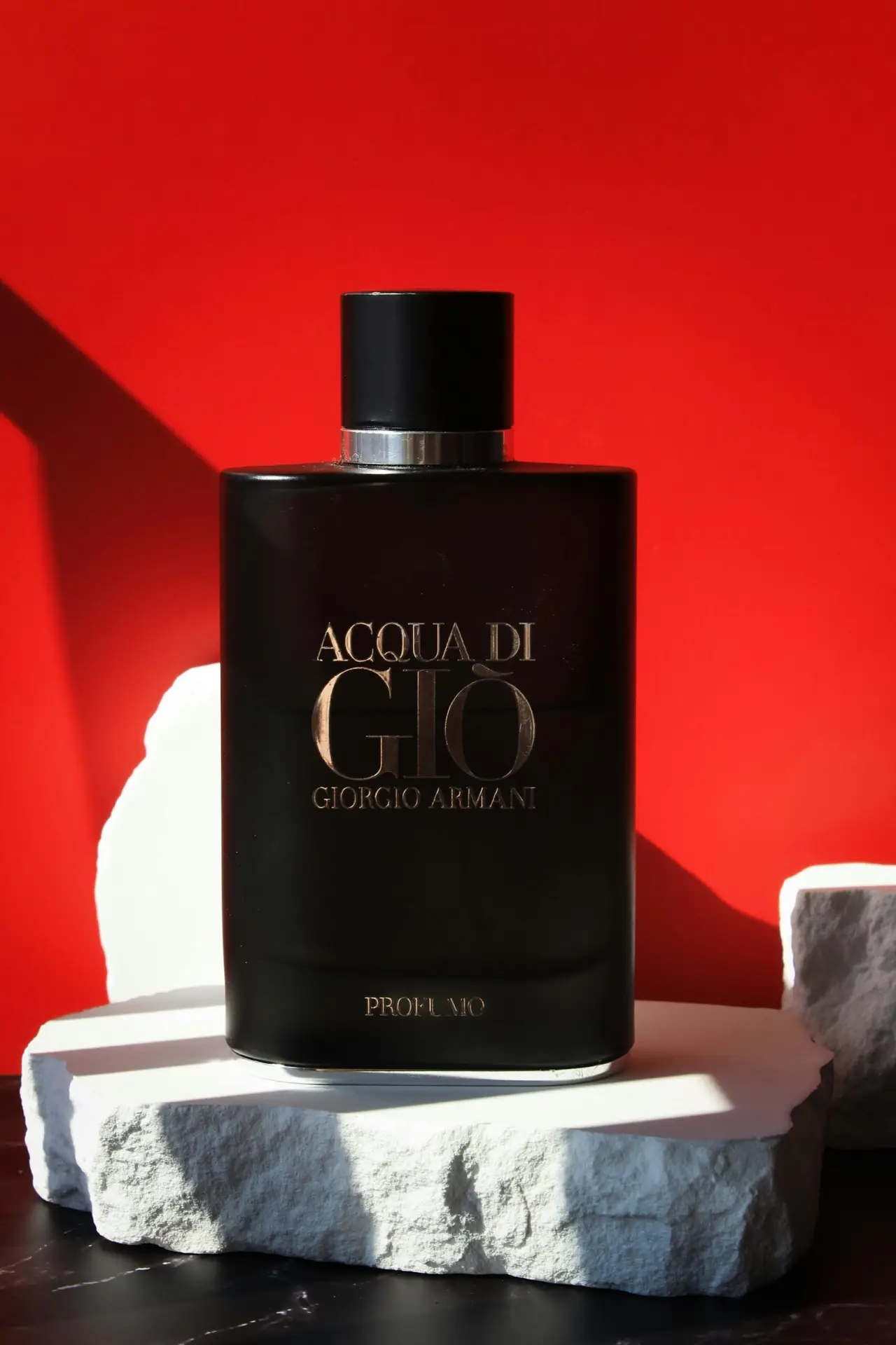 Elegant Acqua Di Gio perfume bottle displayed on stone against vibrant red background.