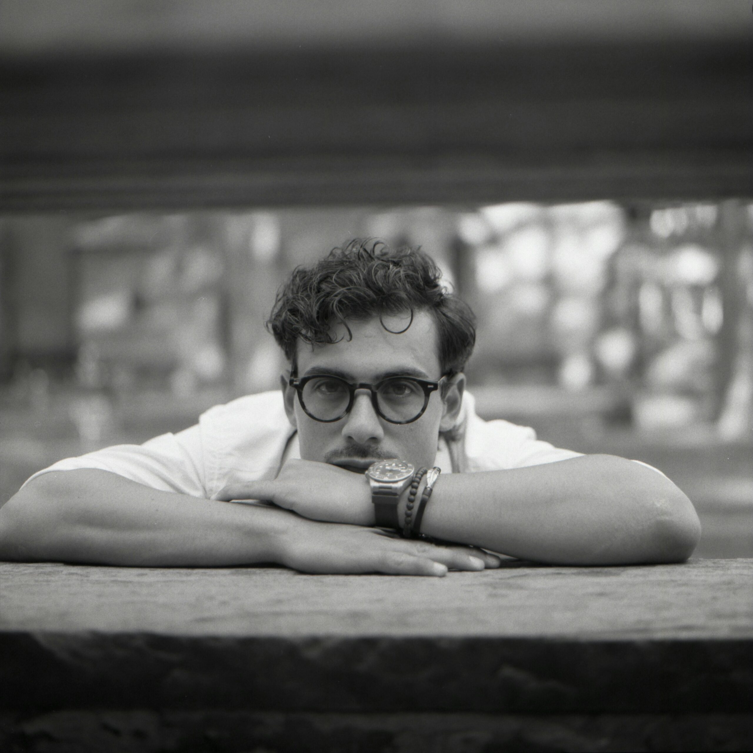 Thoughtful black and white portrait of a man wearing glasses, resting on a stone ledge.