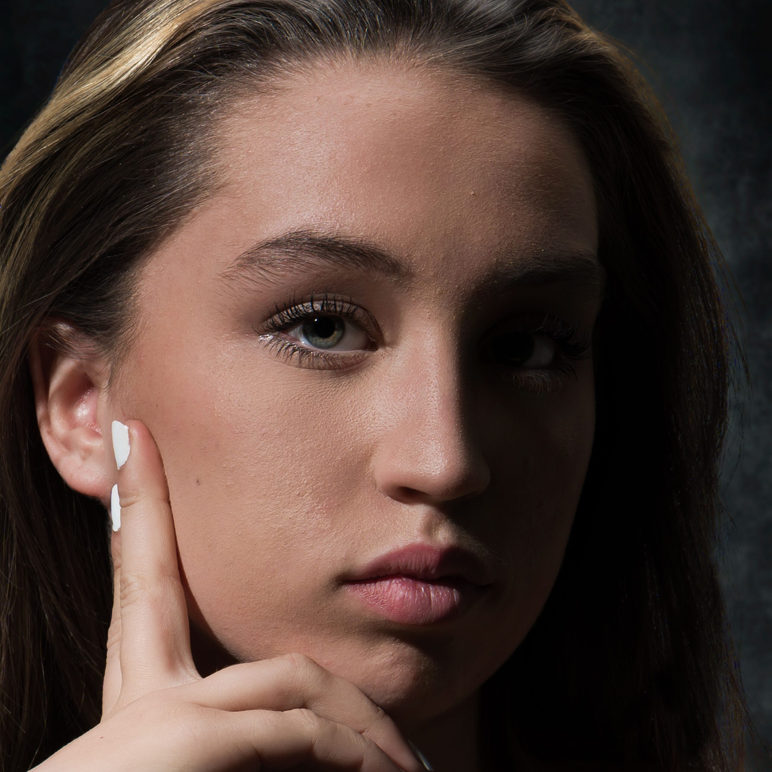 Close-up portrait of a young woman in deep thought, featuring dramatic lighting and a neutral background.