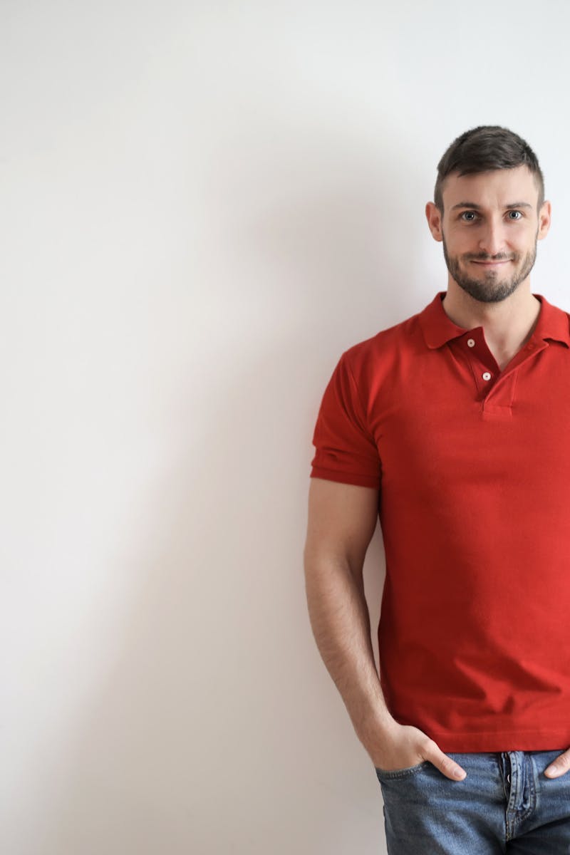 Casually dressed man in red polo stands smiling in front of a white wall.