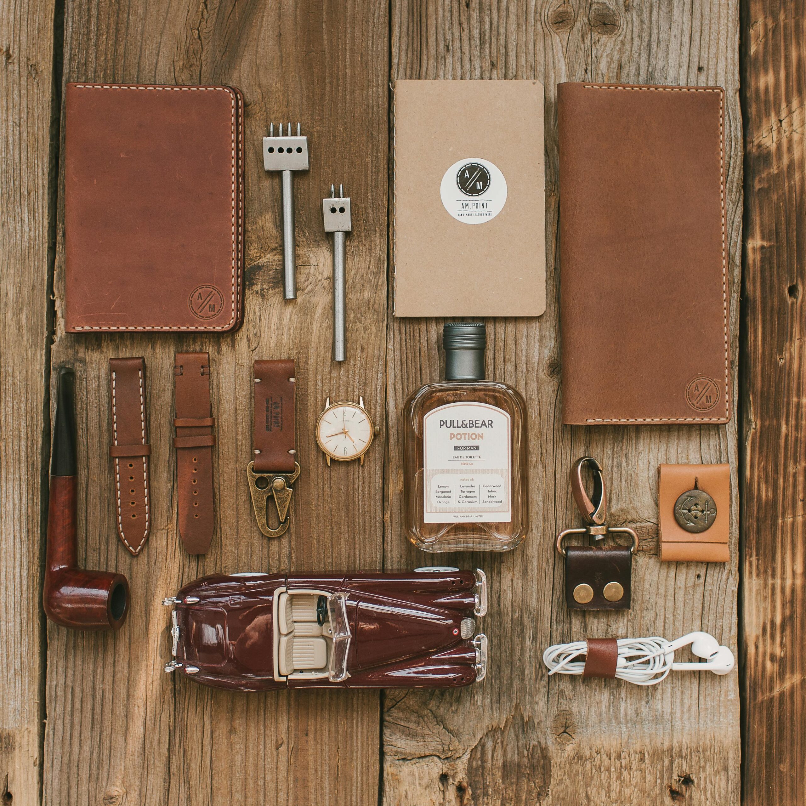 Flat lay showcasing leather accessories, a vintage car model, and modern essentials on a wooden surface.