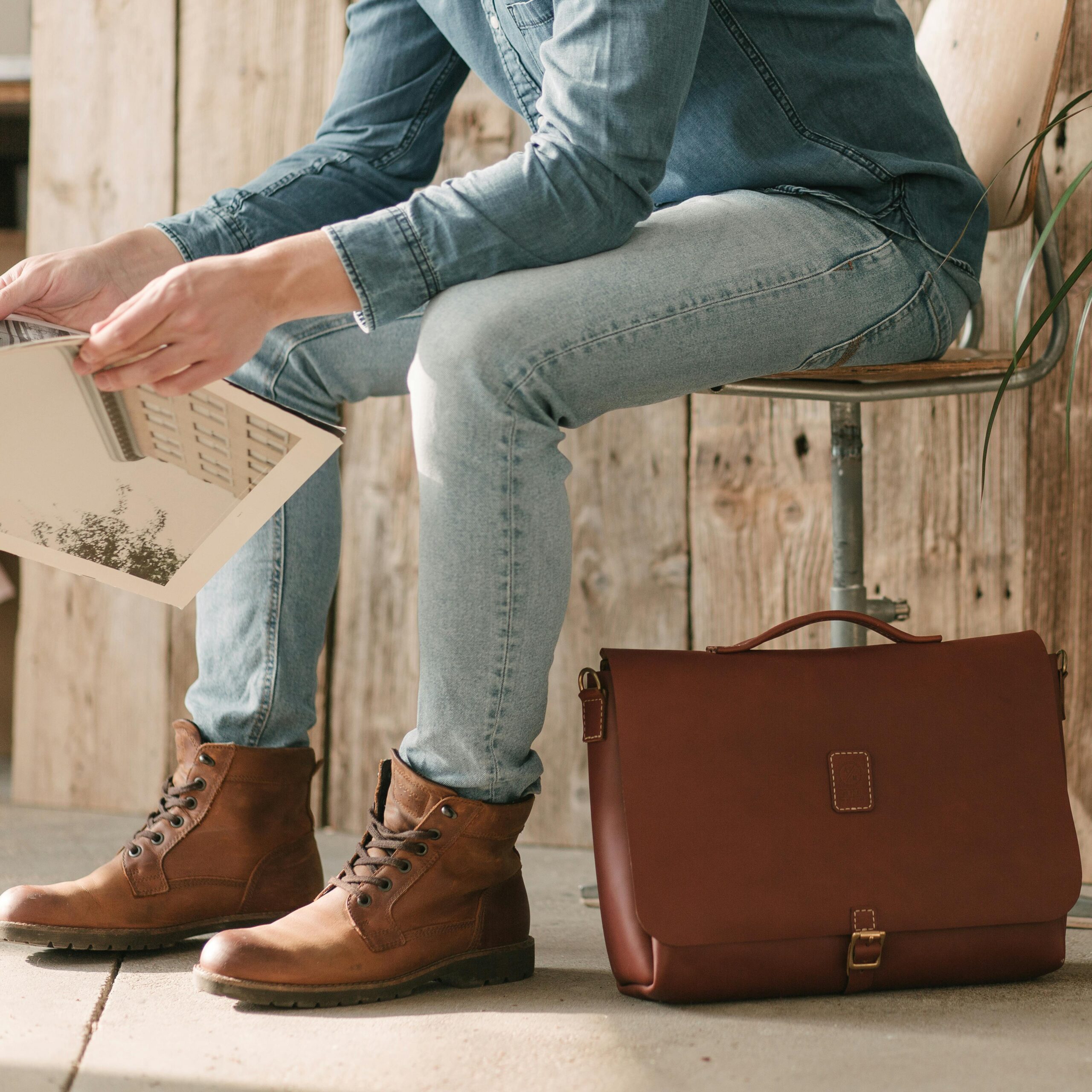 Person sitting on chair with denim outfit, brown leather boots, and a briefcase.