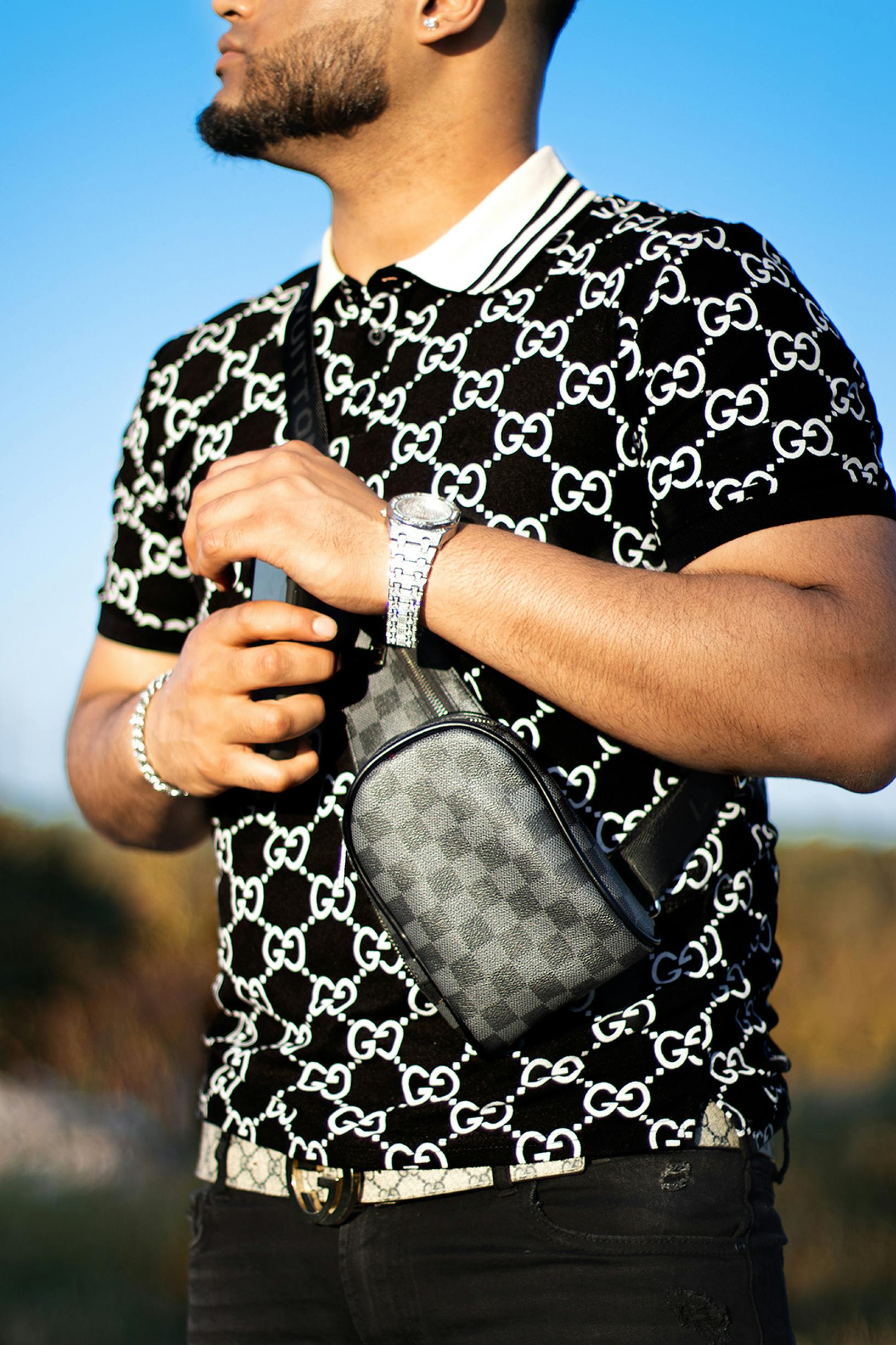 Stylish man wearing designer outfit and crossbody bag with luxury watch, standing outdoors.