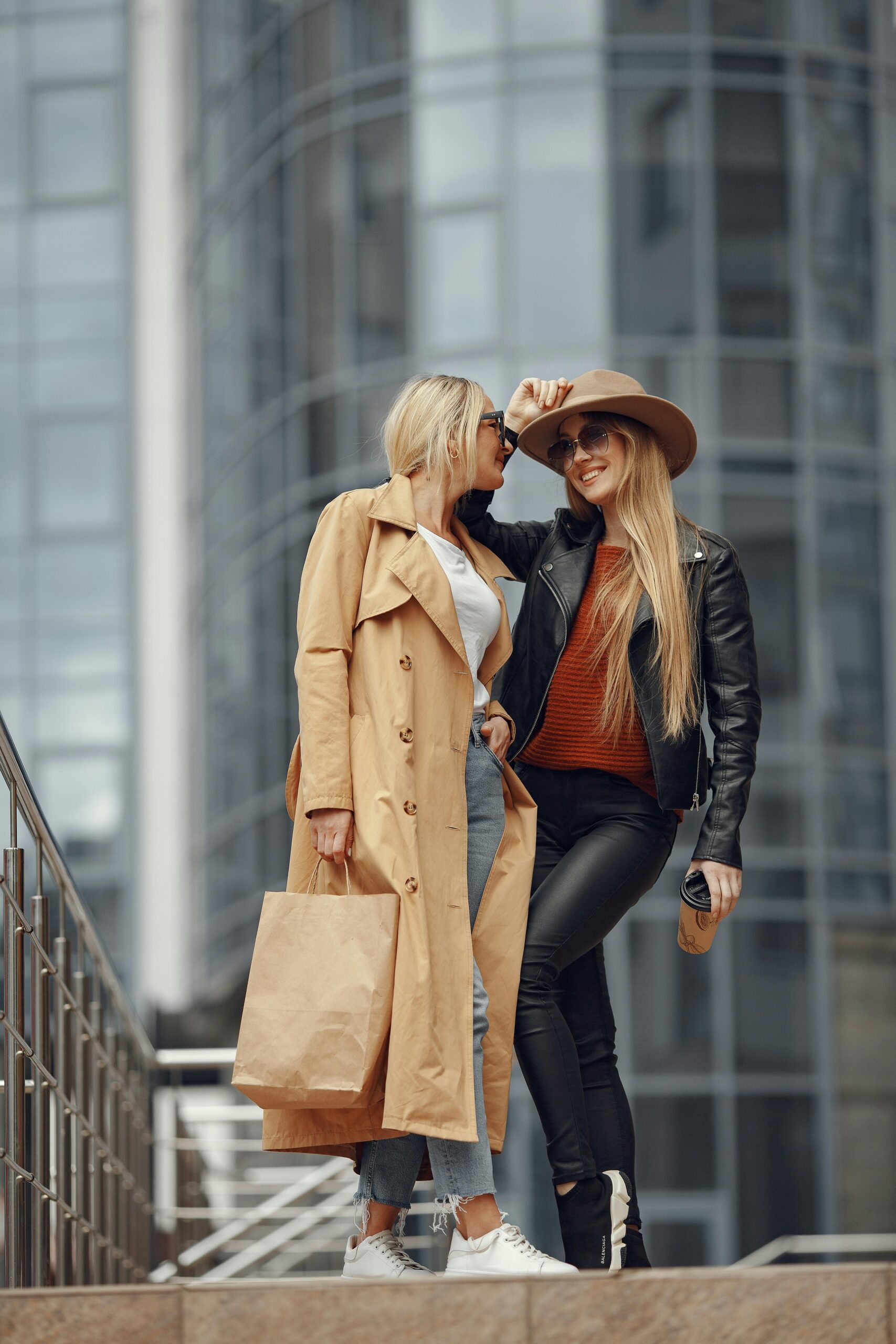 Two fashionable women pose in a city setting, showcasing chic fall outfits.