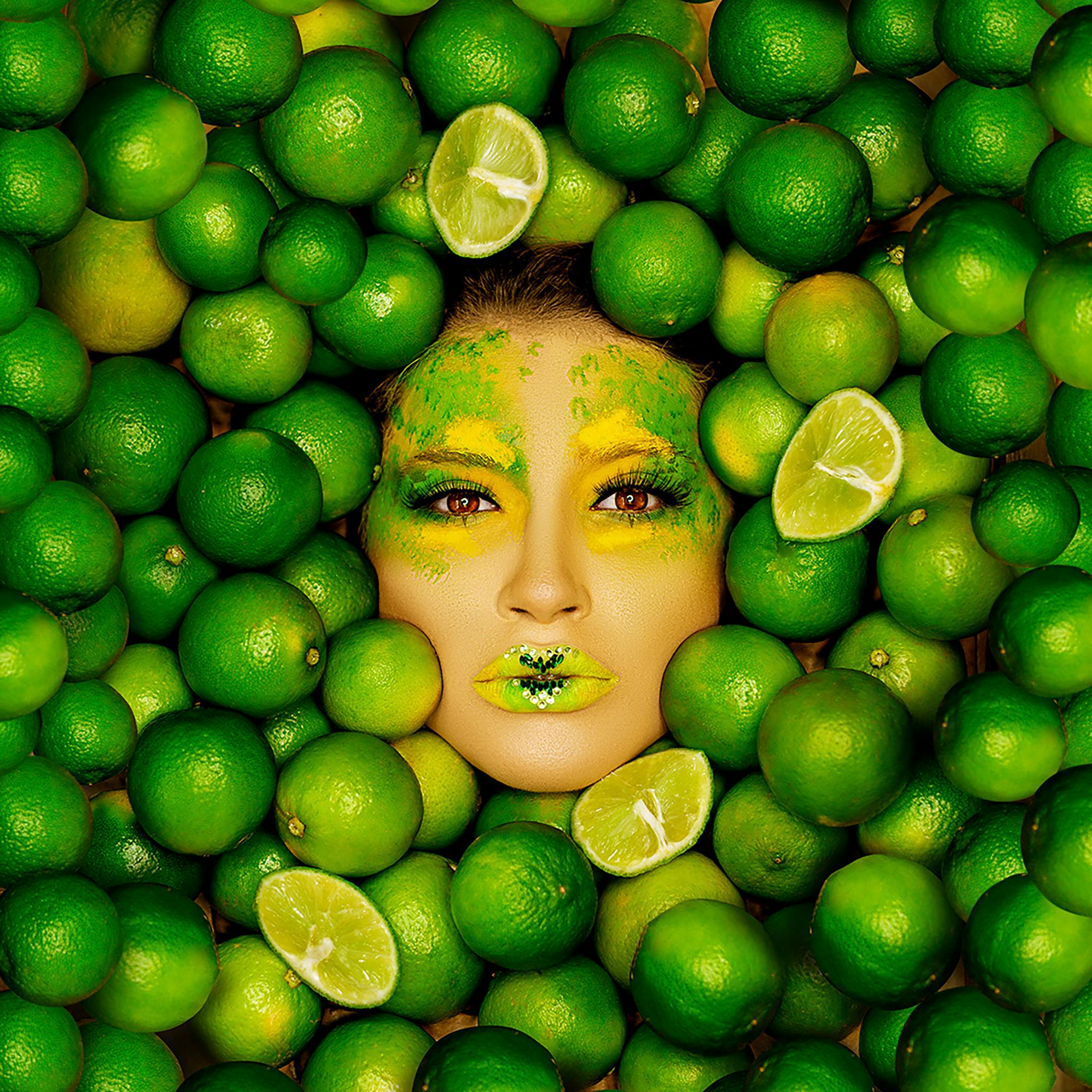 A creative portrait with vivid makeup surrounded by limes, showcasing tropical freshness and color.