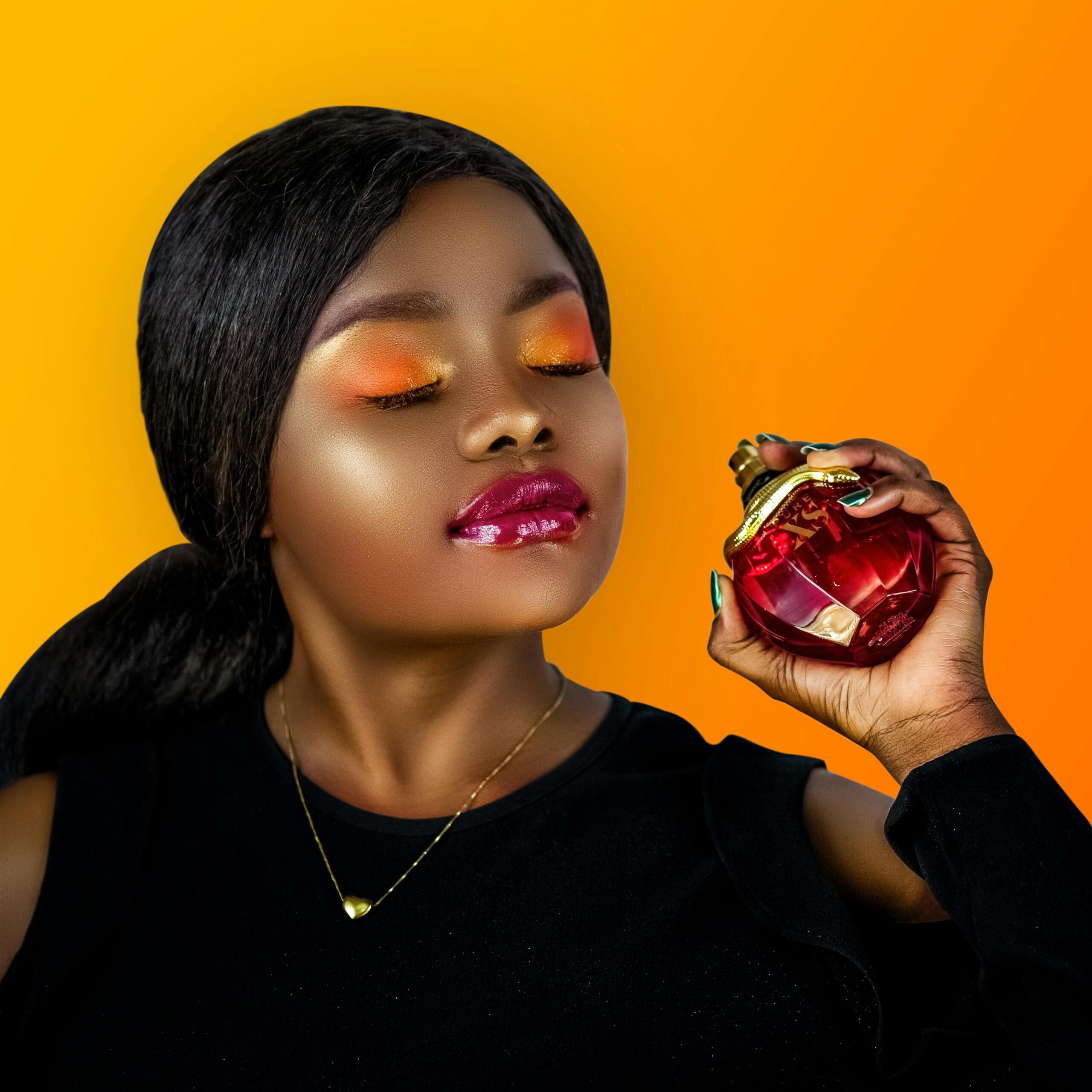 A fashionable woman with vibrant makeup holds a red perfume bottle against an orange background.
