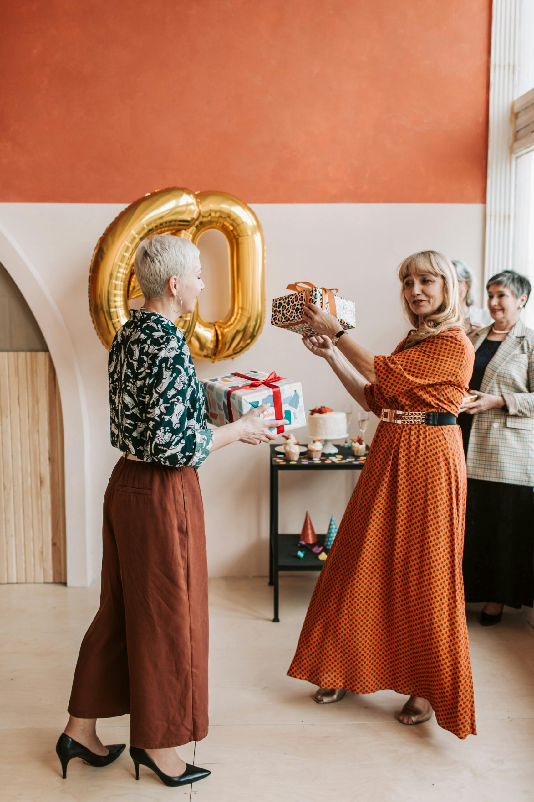 Women in their sixties celebrating a birthday with gifts and joy indoors.