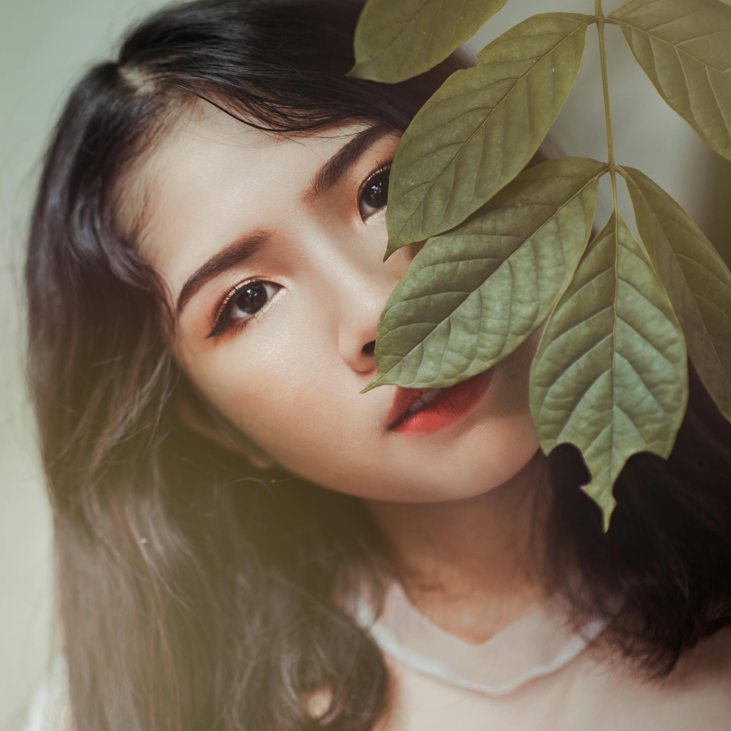 Elegant portrait of a woman behind leaves, highlighting her eyes and red lips.