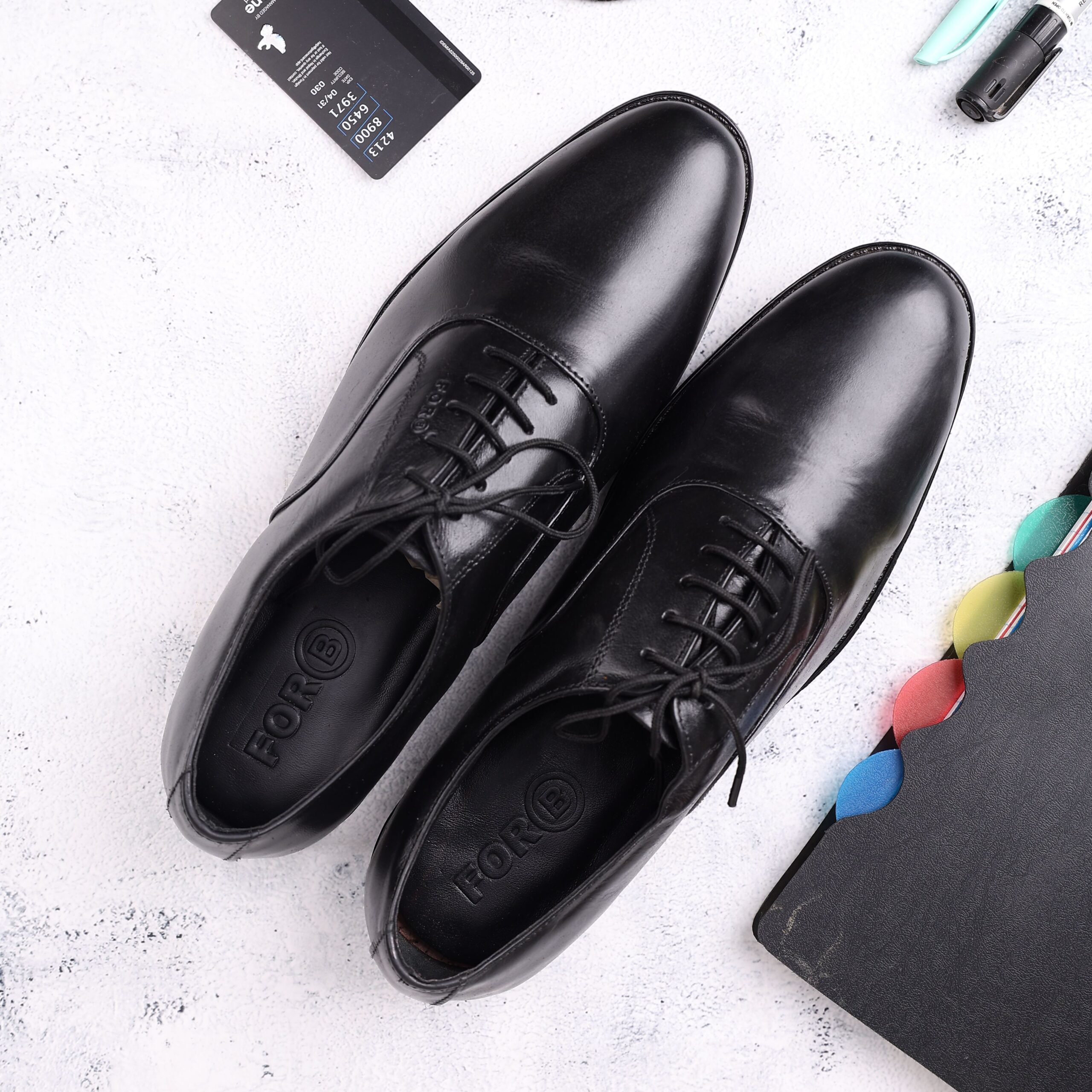Top view of black leather Oxford shoes surrounded by office essentials, ideal for business and fashion themes.