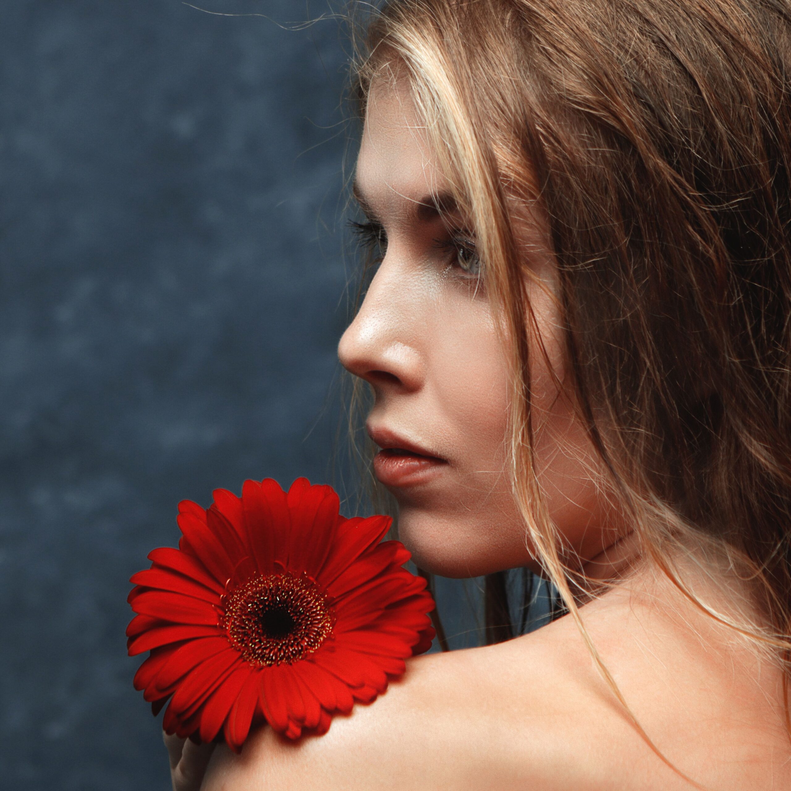A close-up portrait of a woman in profile holding a red gerbera flower.
